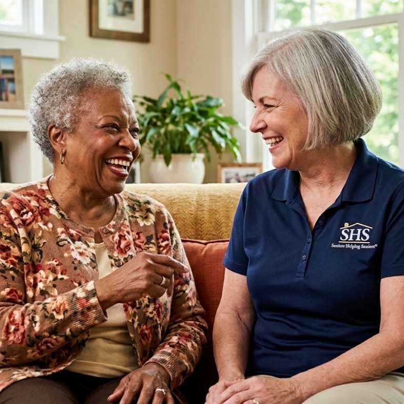 A joyful senior client laughing with a Seniors Helping Seniors Nashville companion caregiver on a living room couch, providing respite care support across Brentwood, Franklin, Bellevue, Donelson, Gallatin, and Mt. Juliet.