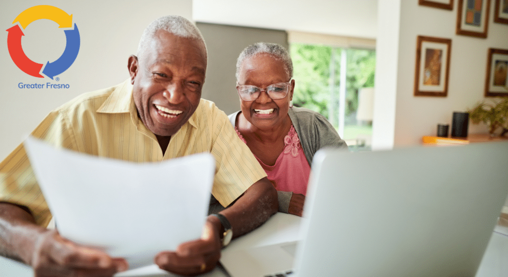 Senior companions sharing a laugh over paperwork and a laptop.