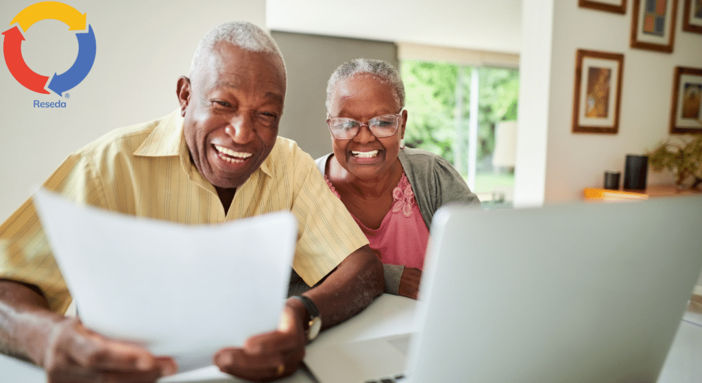 Senior companions sharing a laugh over paperwork and a laptop.