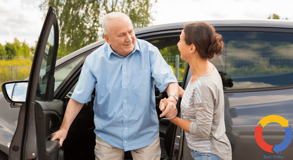 Older man getting out of a car with assistance from a older woman.